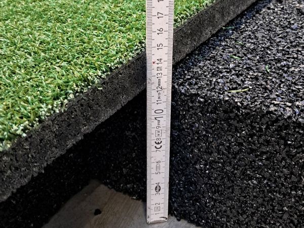 Detailansicht Fallschutz und Rasenmatte mit Zollstock zur Größeneinordnung: Fallschutzschicht 12 cm hoch, Rasenmatte drei cm hoch